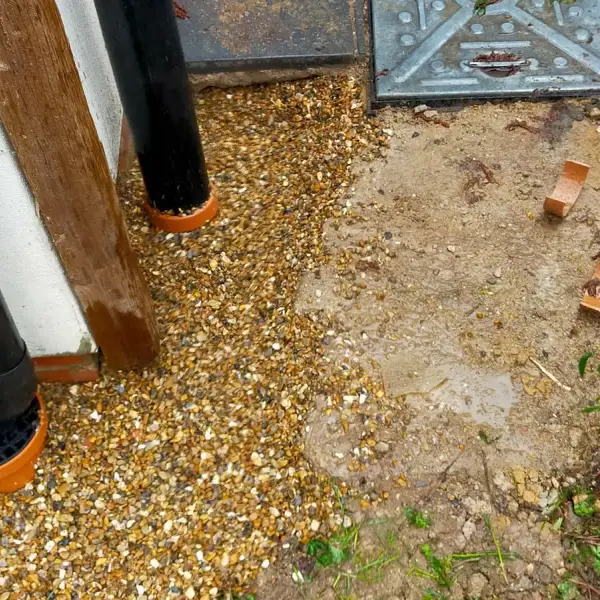New external gully trap fitted under a downpipe beside a manhole cover