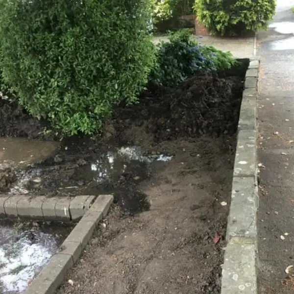 Water from a burst mains supply pooling along a garden edge