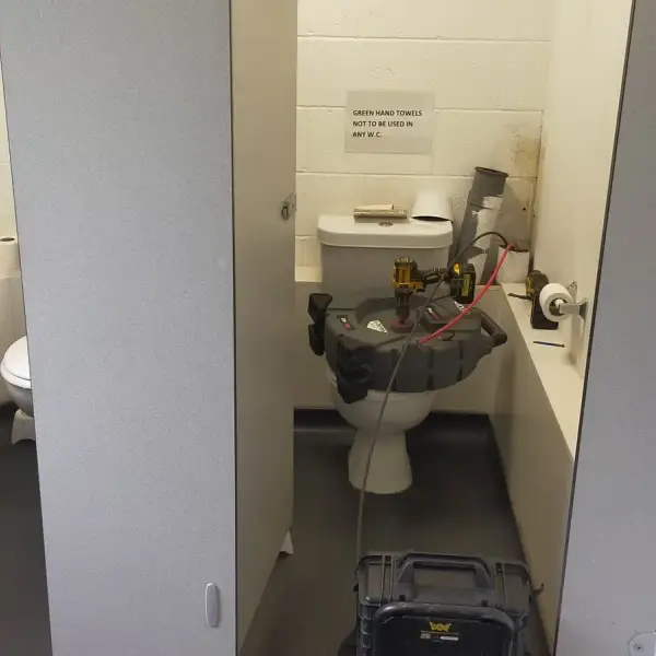 Commercial toilet cubicle with drain clearing machine set up for a blocked drain